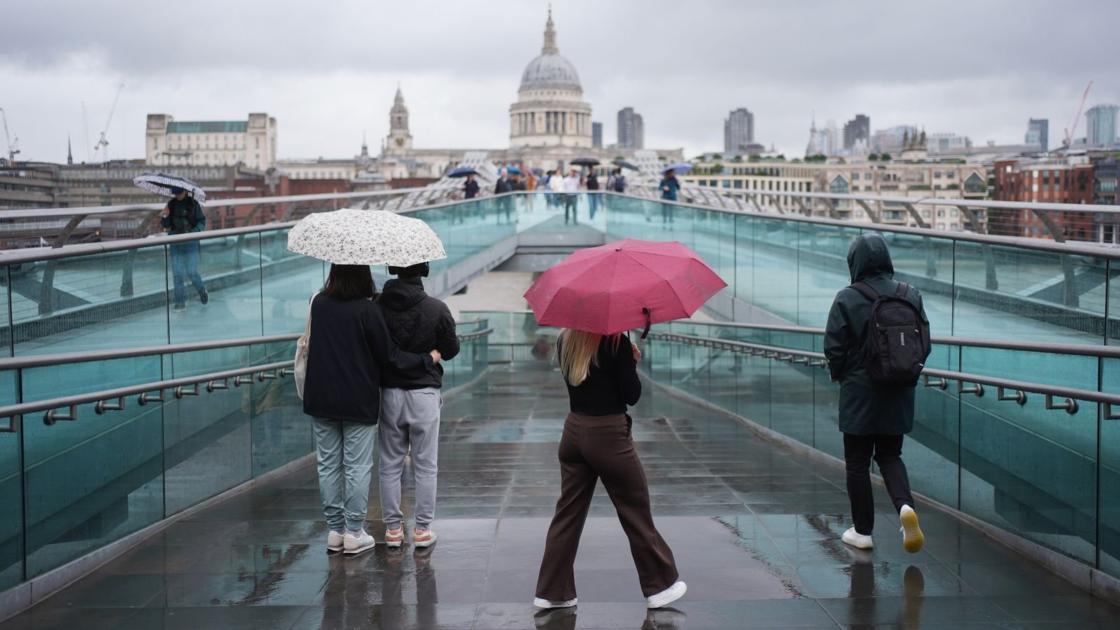 Visitors whip out their umbrellas on Millennium Bridge amid changeable weather earlier this month. Pic: PA